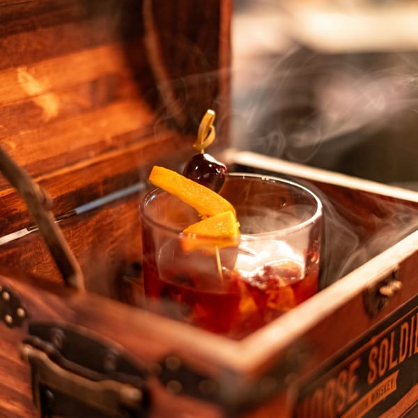 A smoked cocktail with orange peel and cherry in a glass, presented in a wooden box.