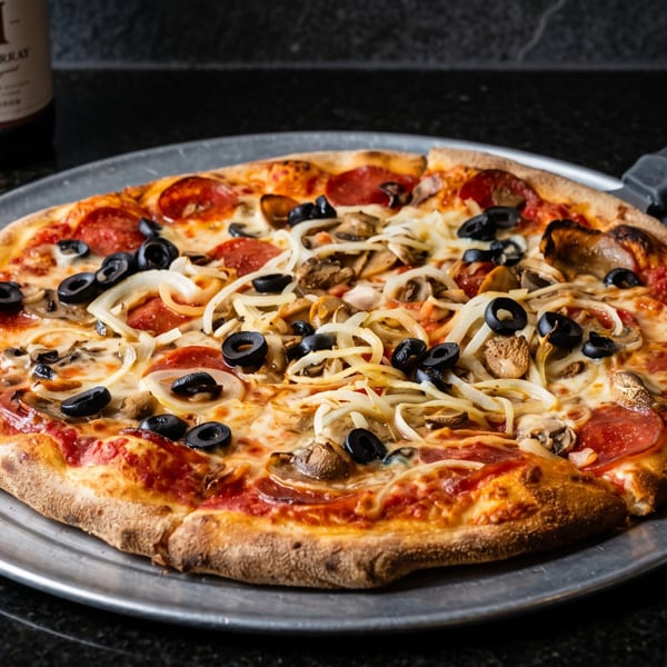 A whole pepperoni, mushroom, onion, and olive pizza on a metal pan with a wine bottle.