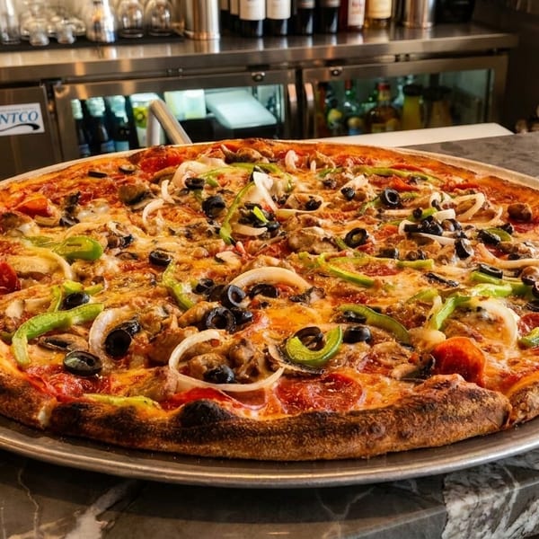 Large, fully loaded pizza with pepperoni, sausage, peppers, onions, and olives on a marble counter.