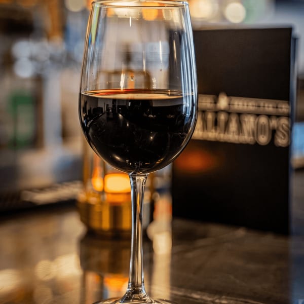 A glass of red wine sits on a dark marble bar, with a menu in the background.