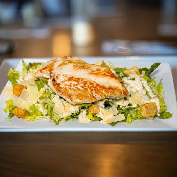 Grilled chicken Caesar salad with romaine lettuce, croutons, parmesan, and creamy dressing on a white plate.