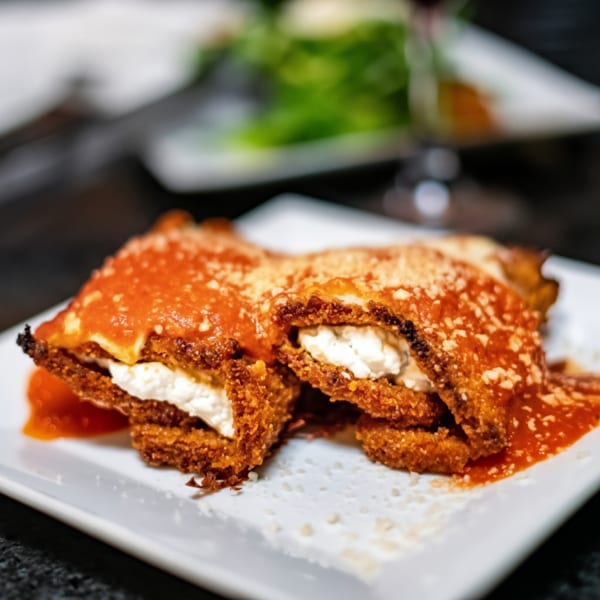 Two pieces of fried eggplant parmesan with ricotta cheese, tomato sauce, and grated cheese.