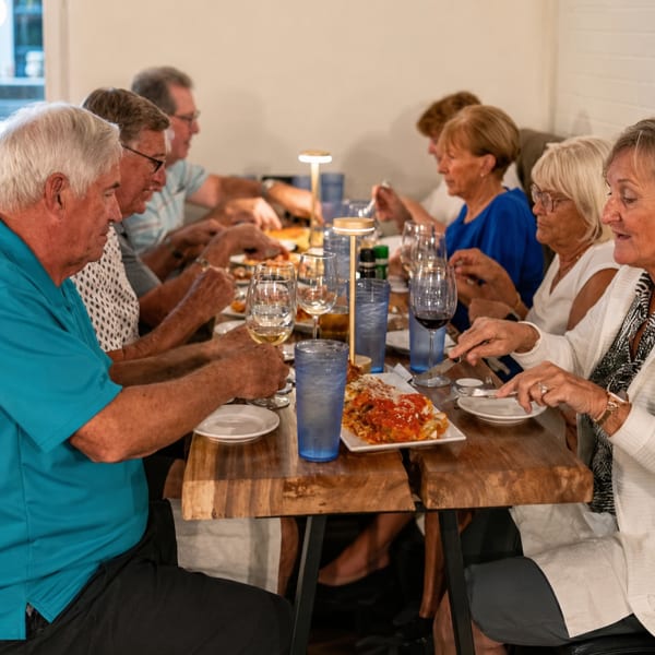 A group of people dining at a long wooden table, enjoying food and drinks.