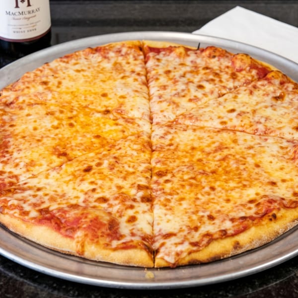 A large cheese pizza on a metal tray, with a bottle of wine and napkins in the background.