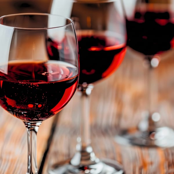 Three glasses of red wine on a wooden table, with the closest glass in sharp focus.