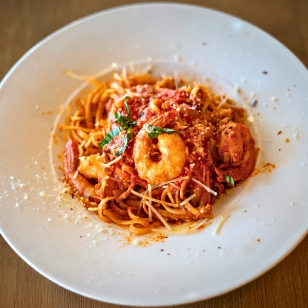 Shrimp linguine pasta with red sauce, parmesan cheese, and basil on a white plate.
