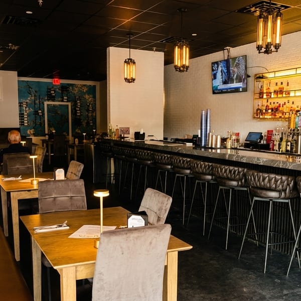 A modern restaurant interior with a long bar, booth seating, and a few patrons dining.