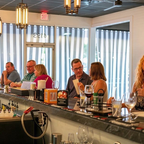Patrons seated at a long bar in a brightly lit restaurant, enjoying drinks and conversation.
