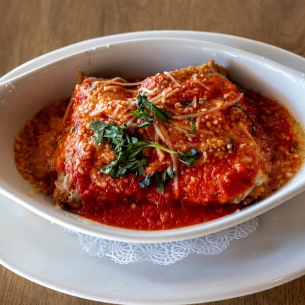 Baked lasagna in a white dish, topped with red sauce, melted cheese, and fresh basil.