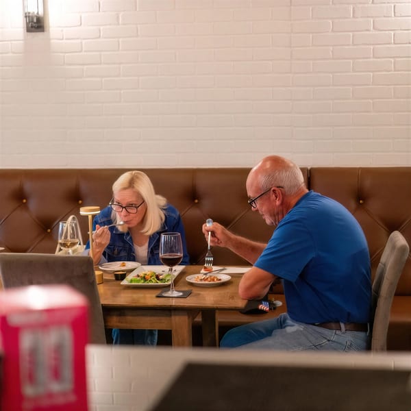 Two people dining at a restaurant, enjoying meals and drinks at a wooden table.