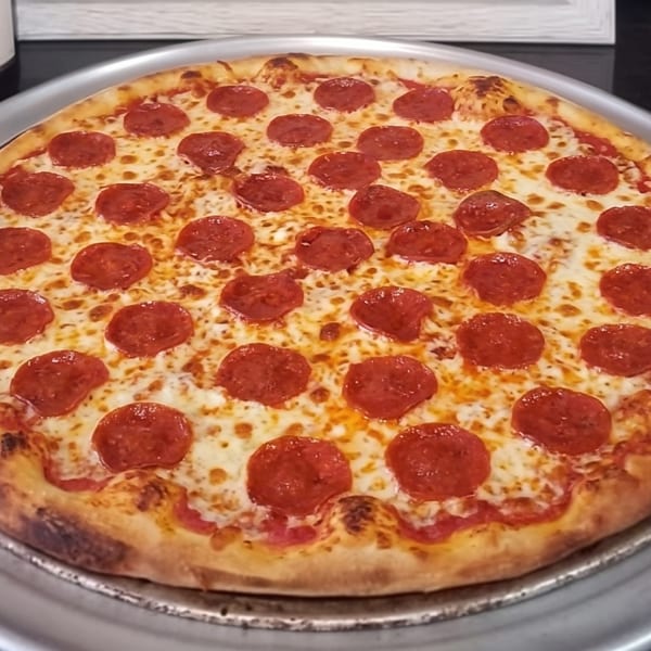 A whole pepperoni pizza with melted cheese on a metal tray, with a wine bottle in the background.